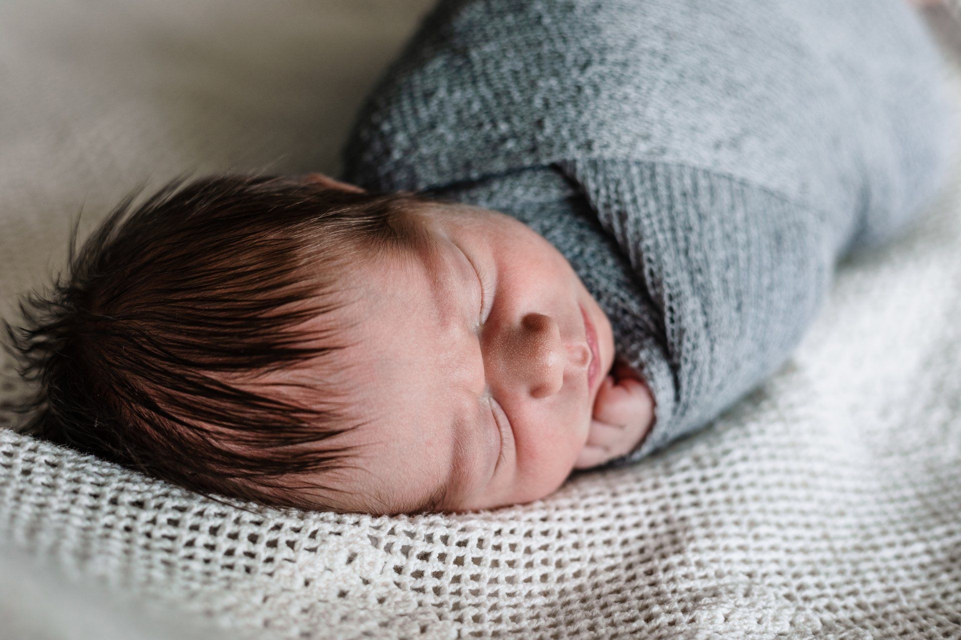 A newborn baby wrapped in a blanket is sleeping on a blanket.