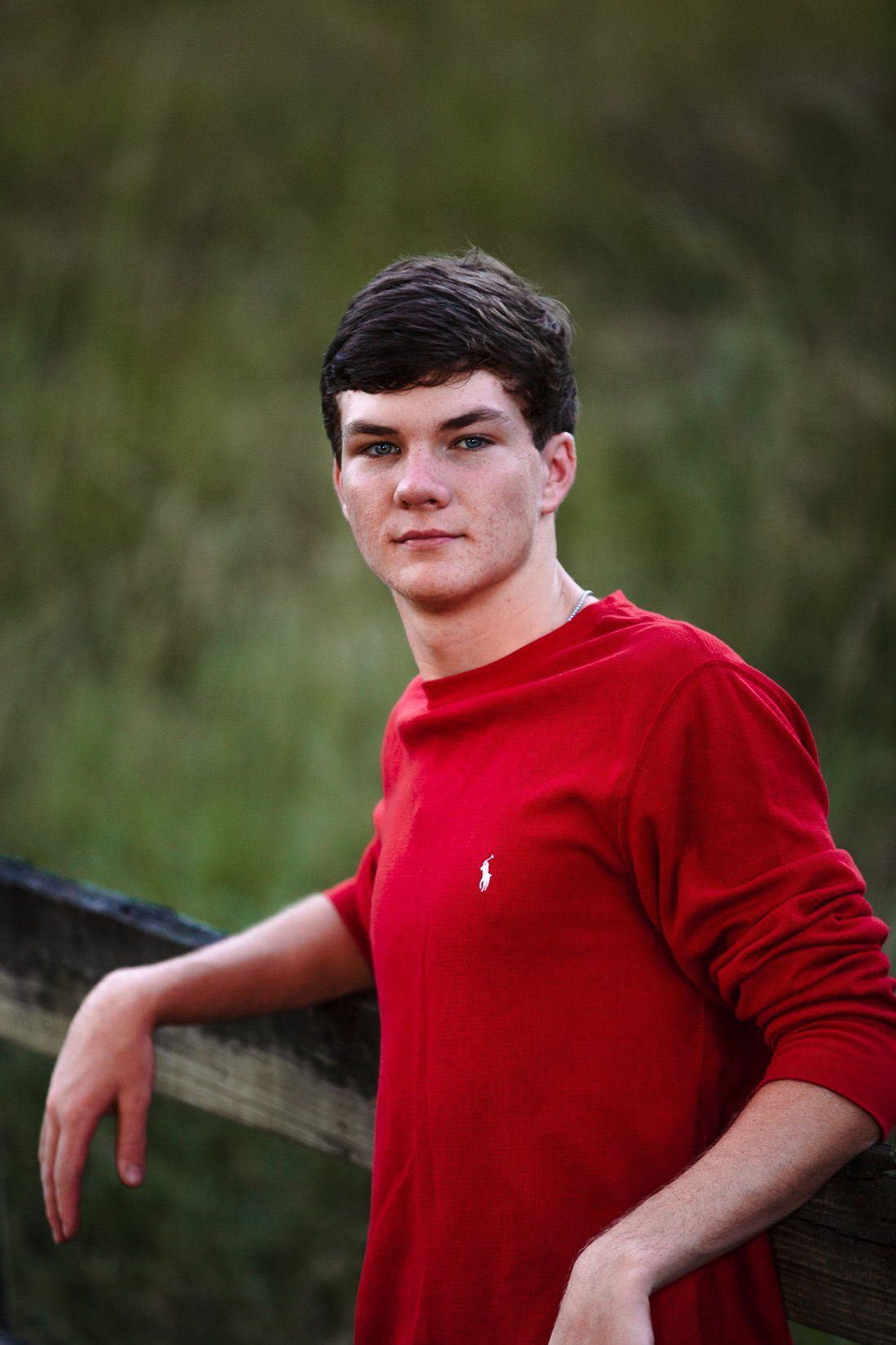 A young man in a red shirt is leaning against a wooden fence.
