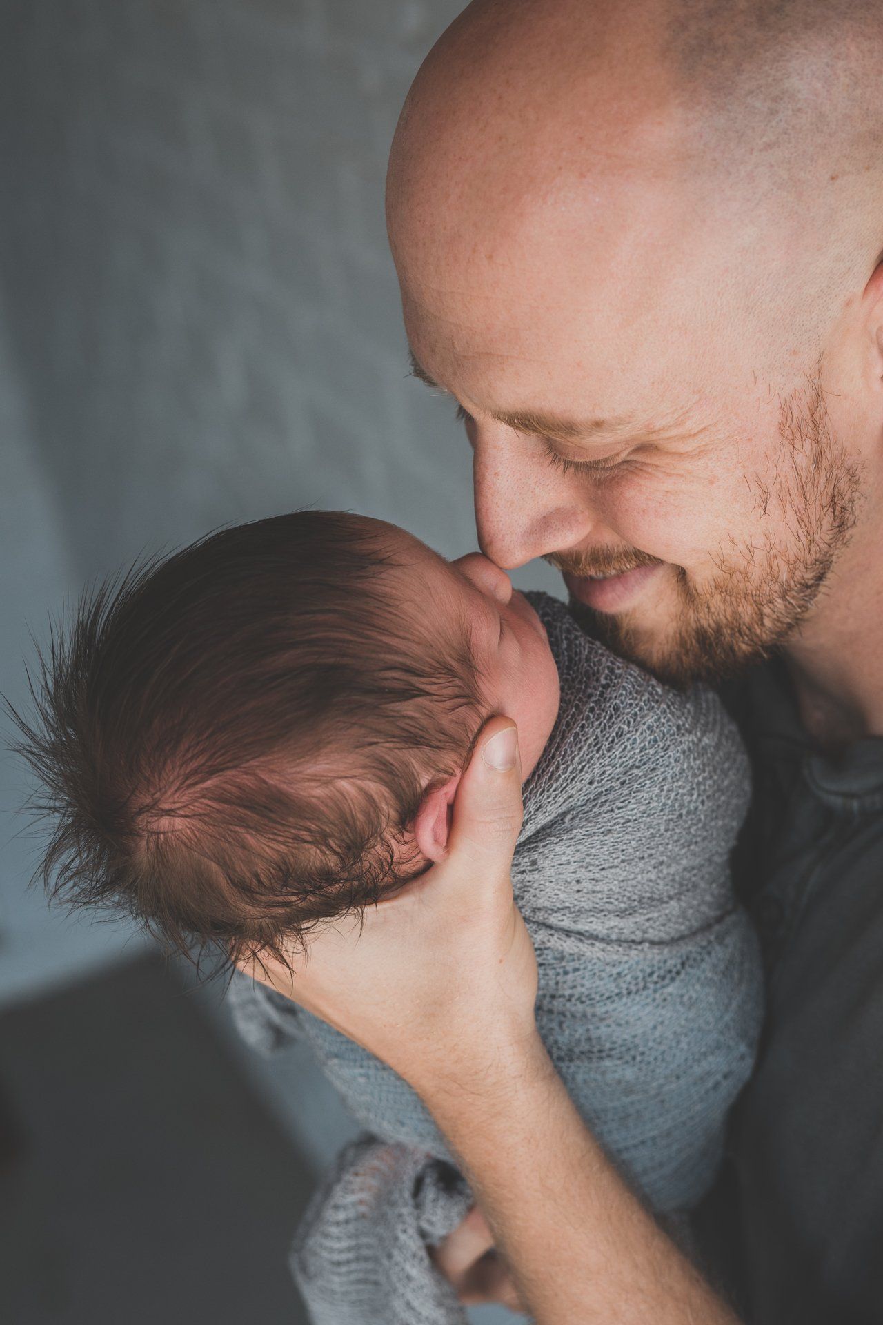 Man holding newborn baby wrapped in grey cloth.