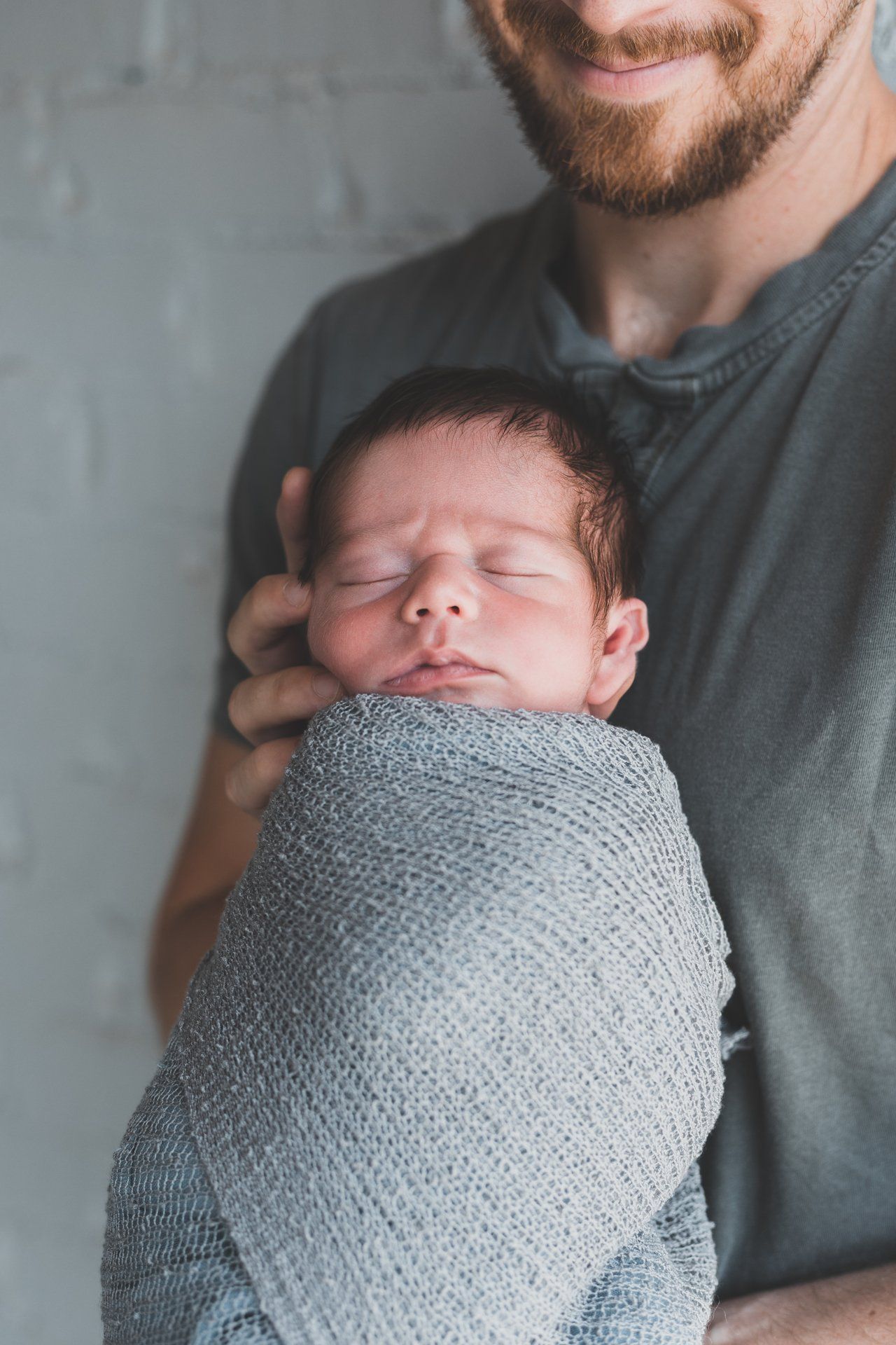A man is holding a newborn baby wrapped in a blanket.