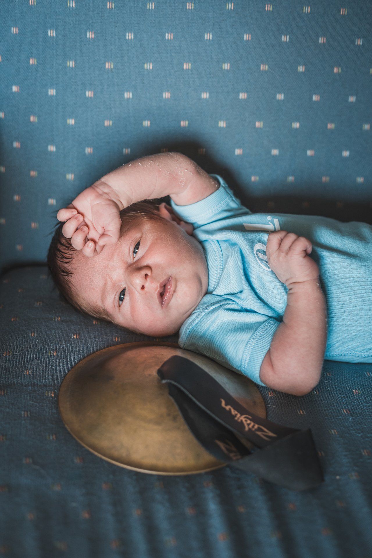 A baby is laying on a bed next to a drum.