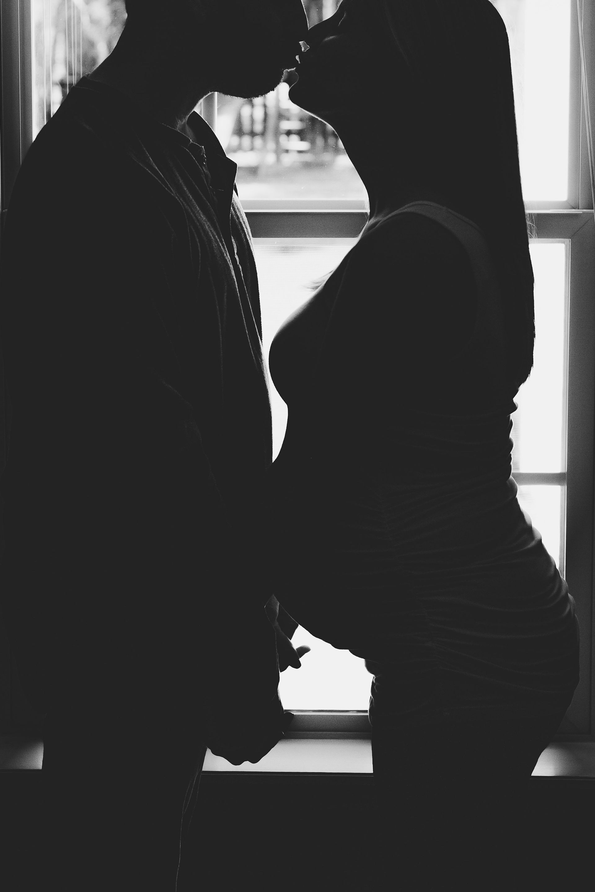 A man and a woman are kissing in front of a window.