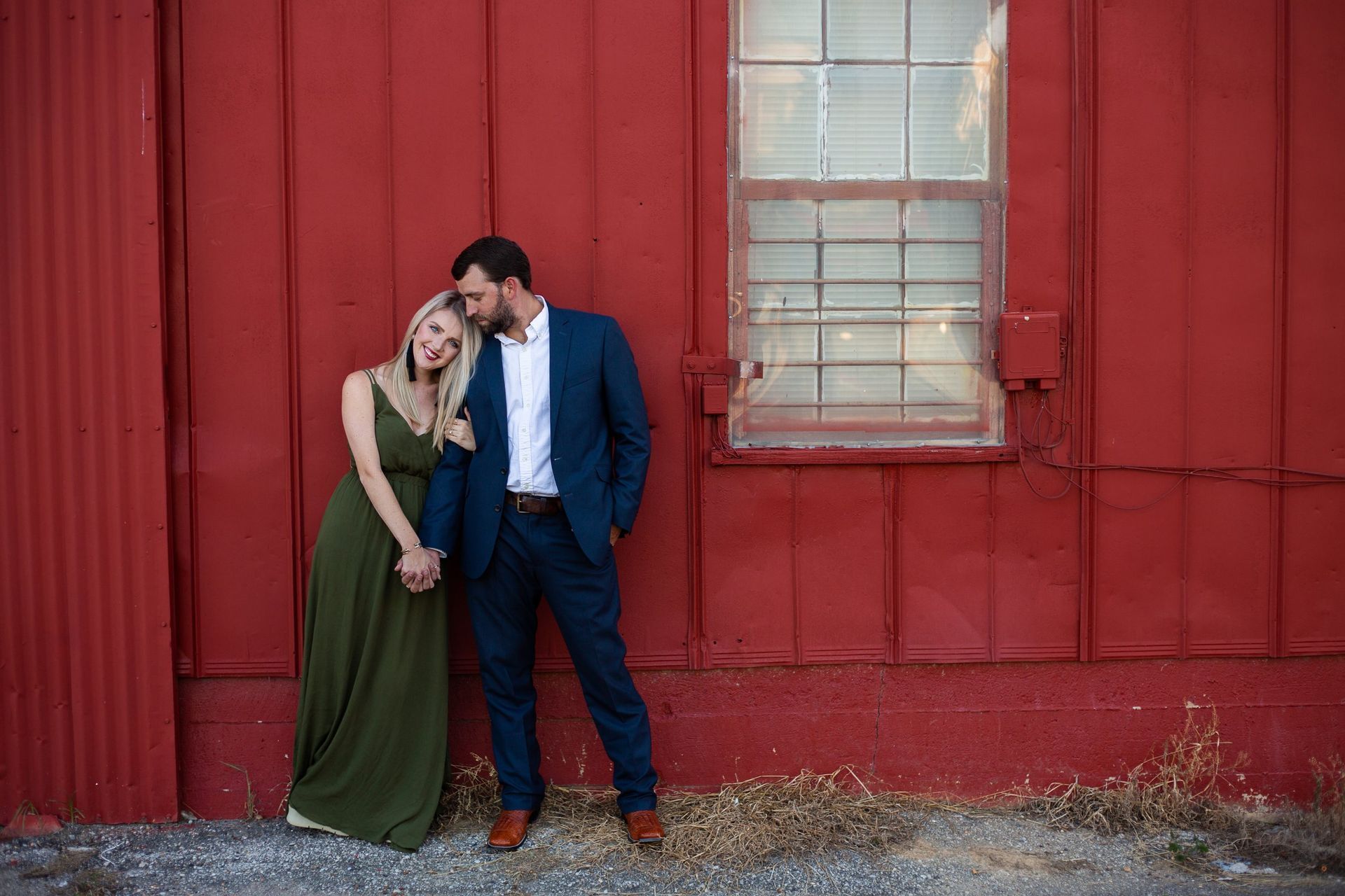 A man and a woman are standing in front of a red building holding hands.