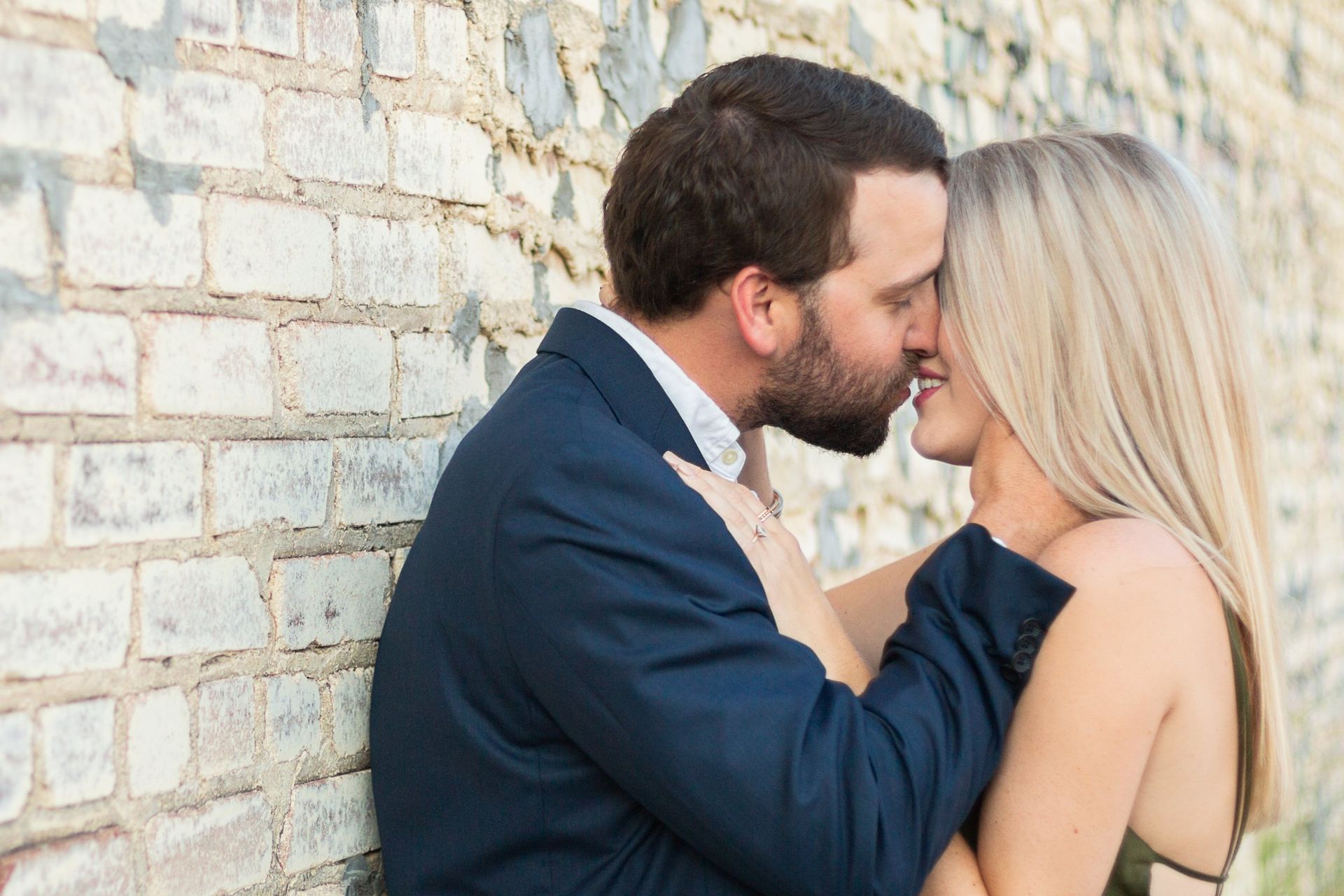 A man and a woman are kissing in front of a brick wall.