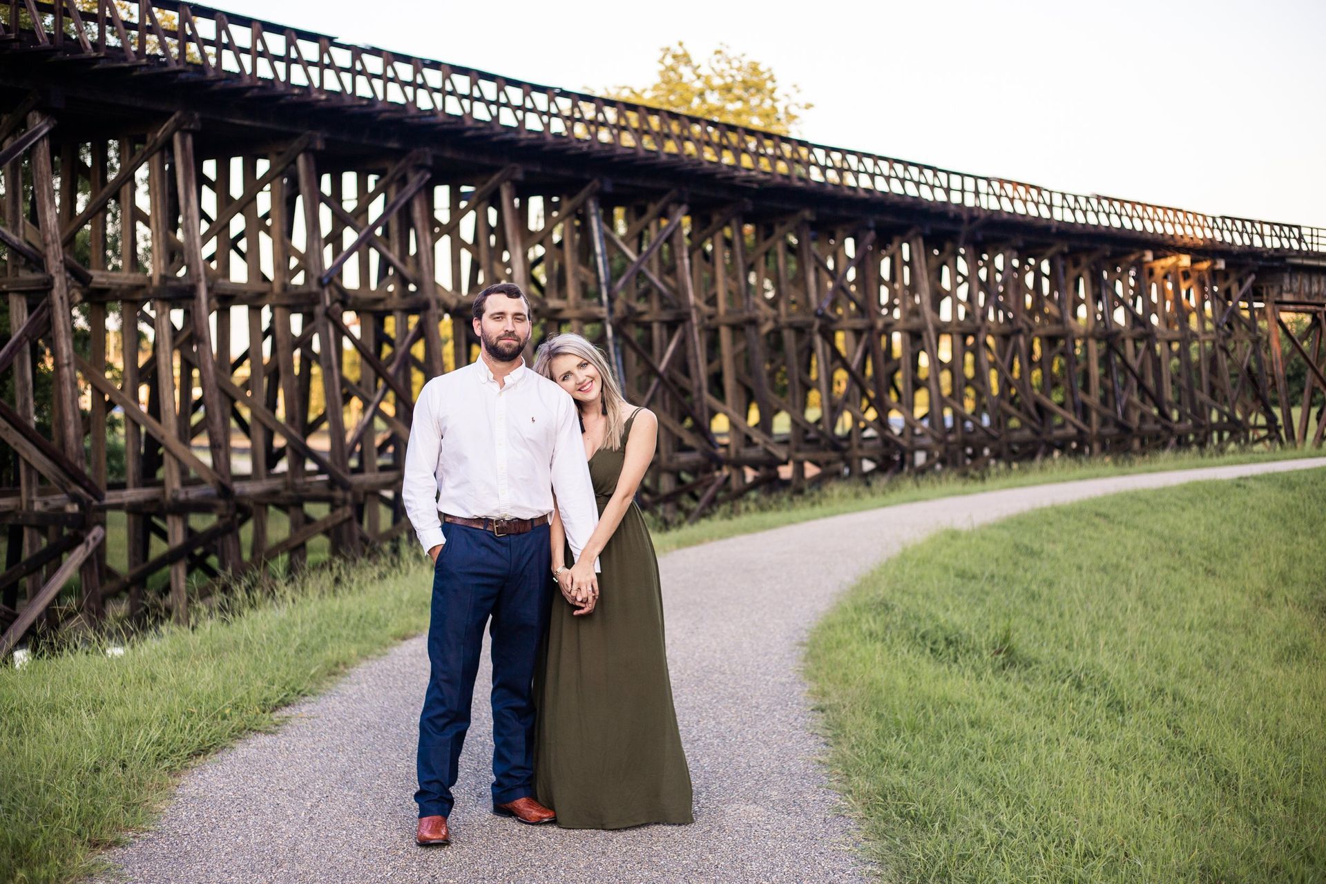 A man and a woman are standing next to each other on a path in front of a wooden bridge.