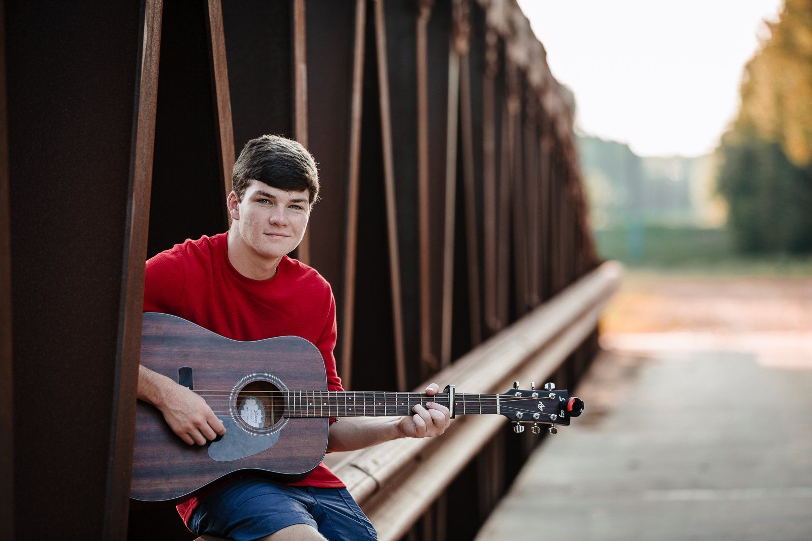 A young man is sitting on a bridge holding an acoustic guitar.