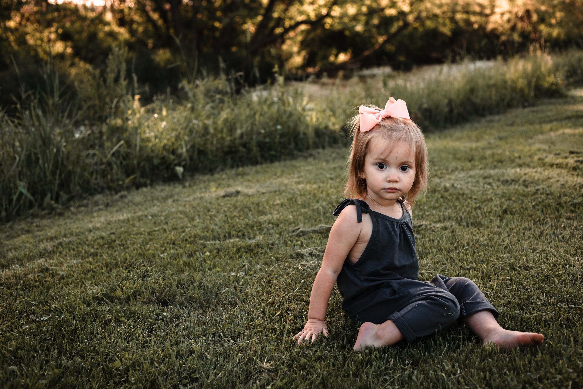 A little girl is sitting on the grass in a field.
