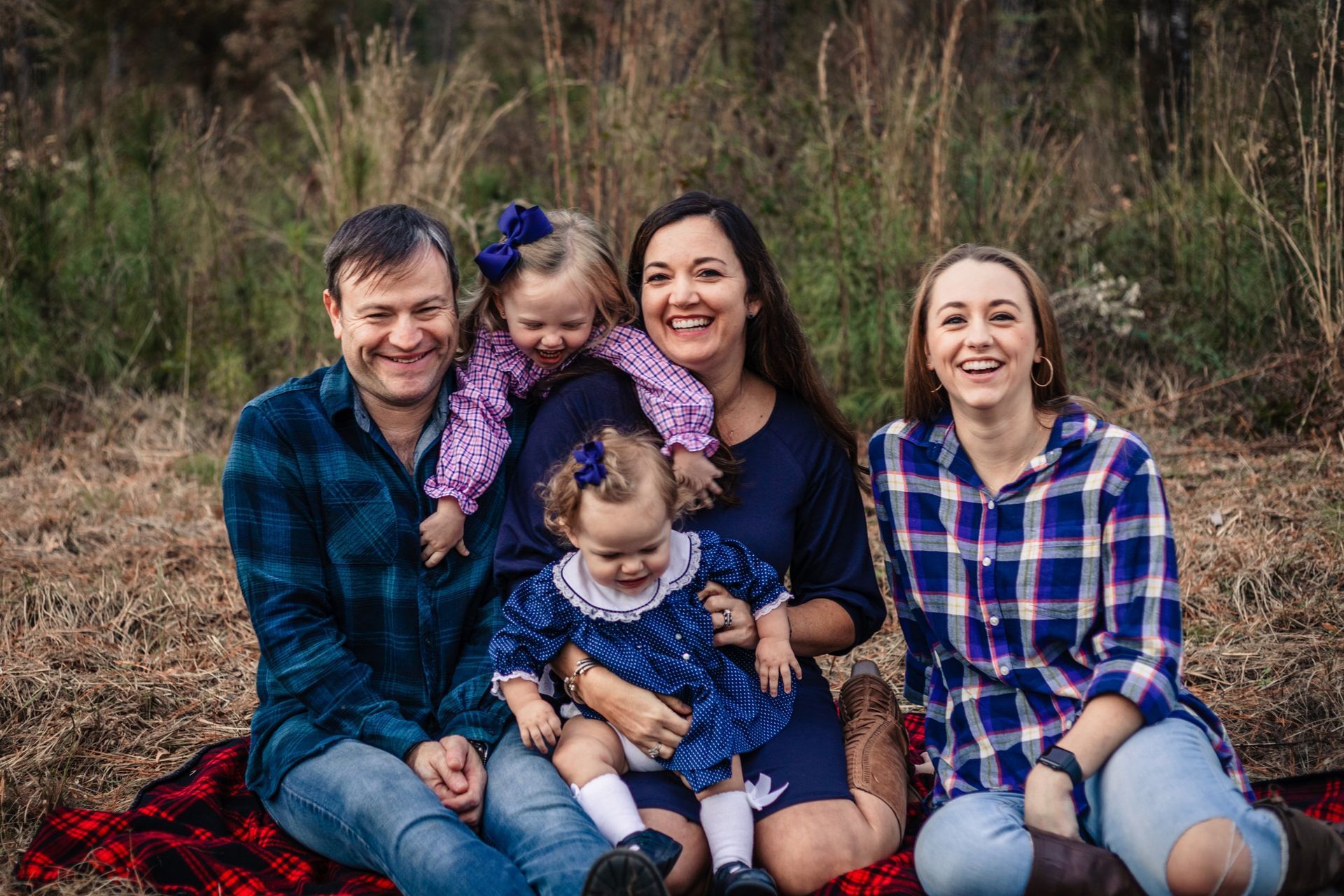 A family is posing for a picture while sitting on a blanket in a field.