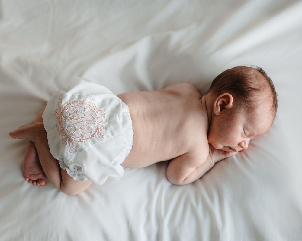 A newborn baby in a diaper is sleeping on a bed.