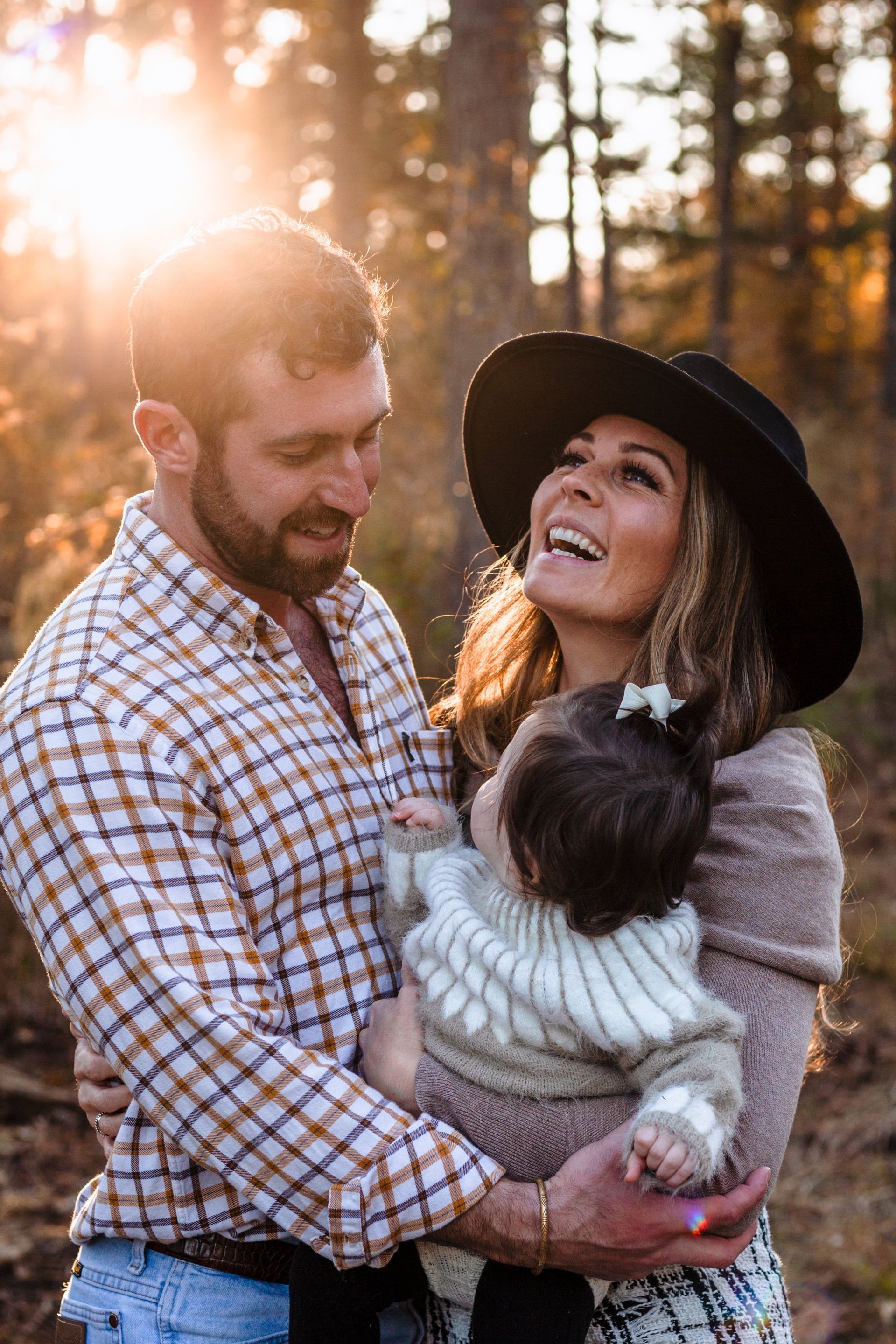 A man and a woman are holding a baby in the woods.