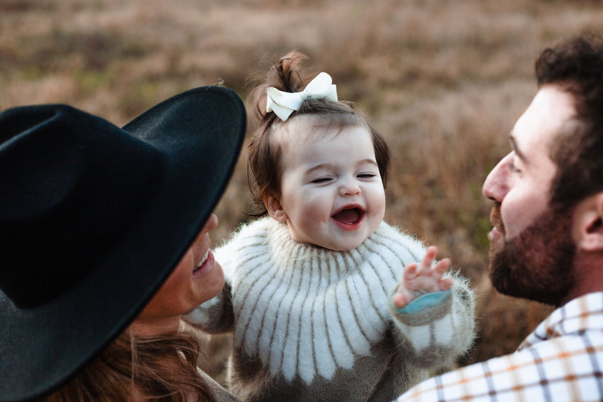 A man and woman are holding a baby girl in a field.