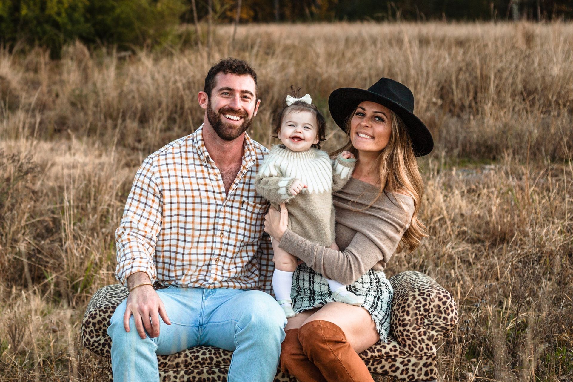 A family is posing for a picture while sitting on a chair in a field.