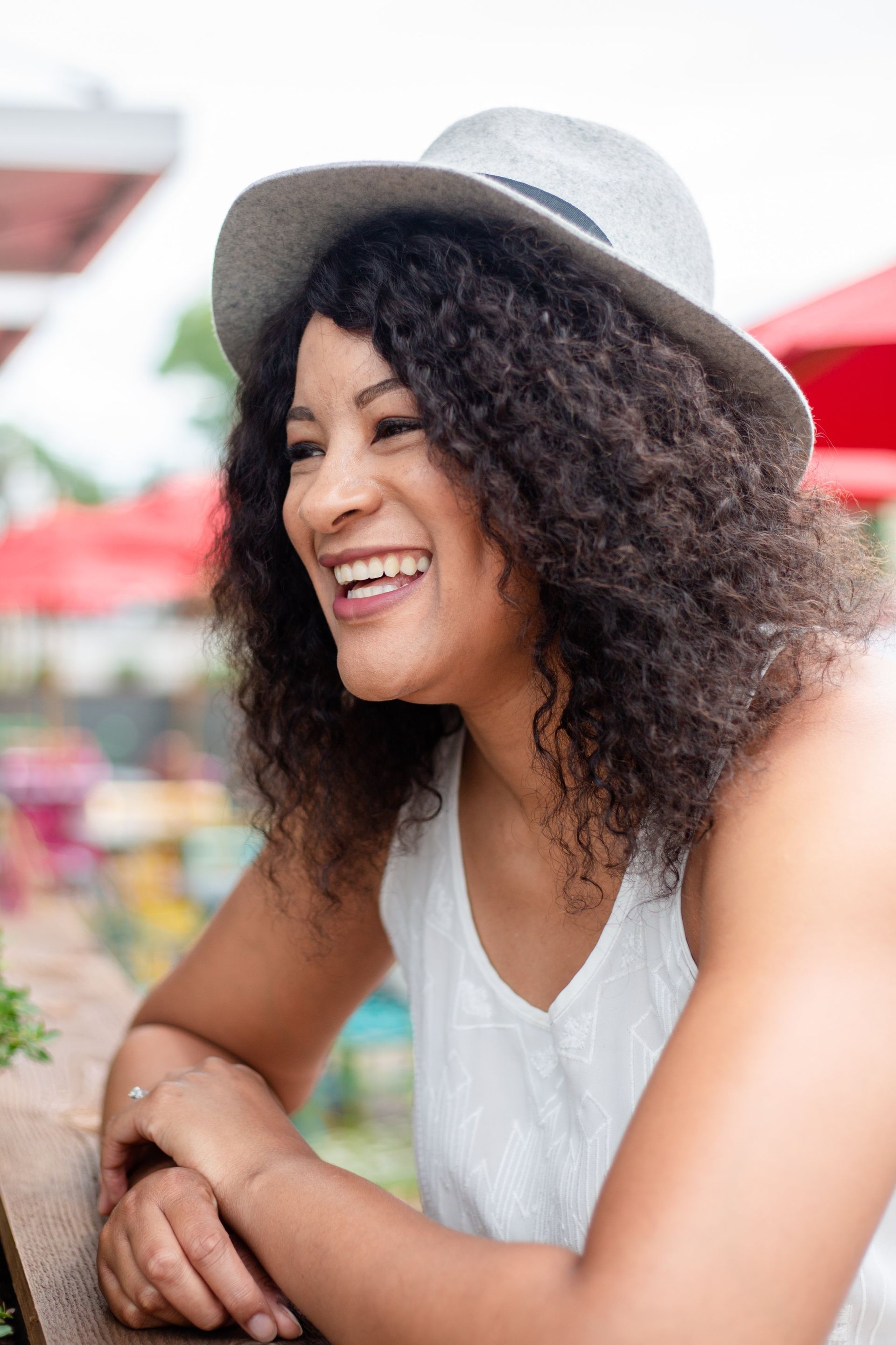 A woman wearing a hat and a white tank top is smiling.