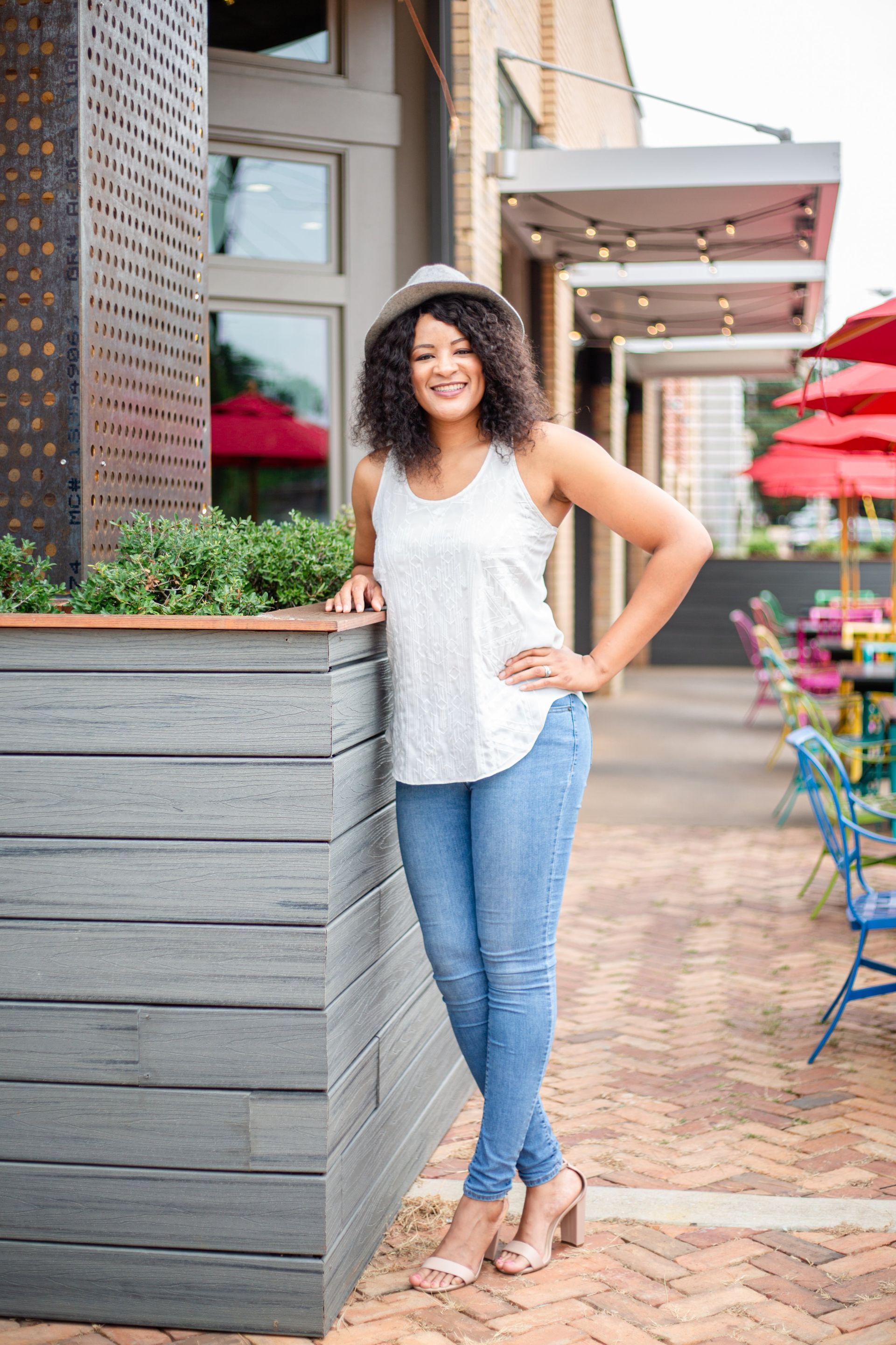 A woman in a white tank top and blue jeans is standing in front of a restaurant.
