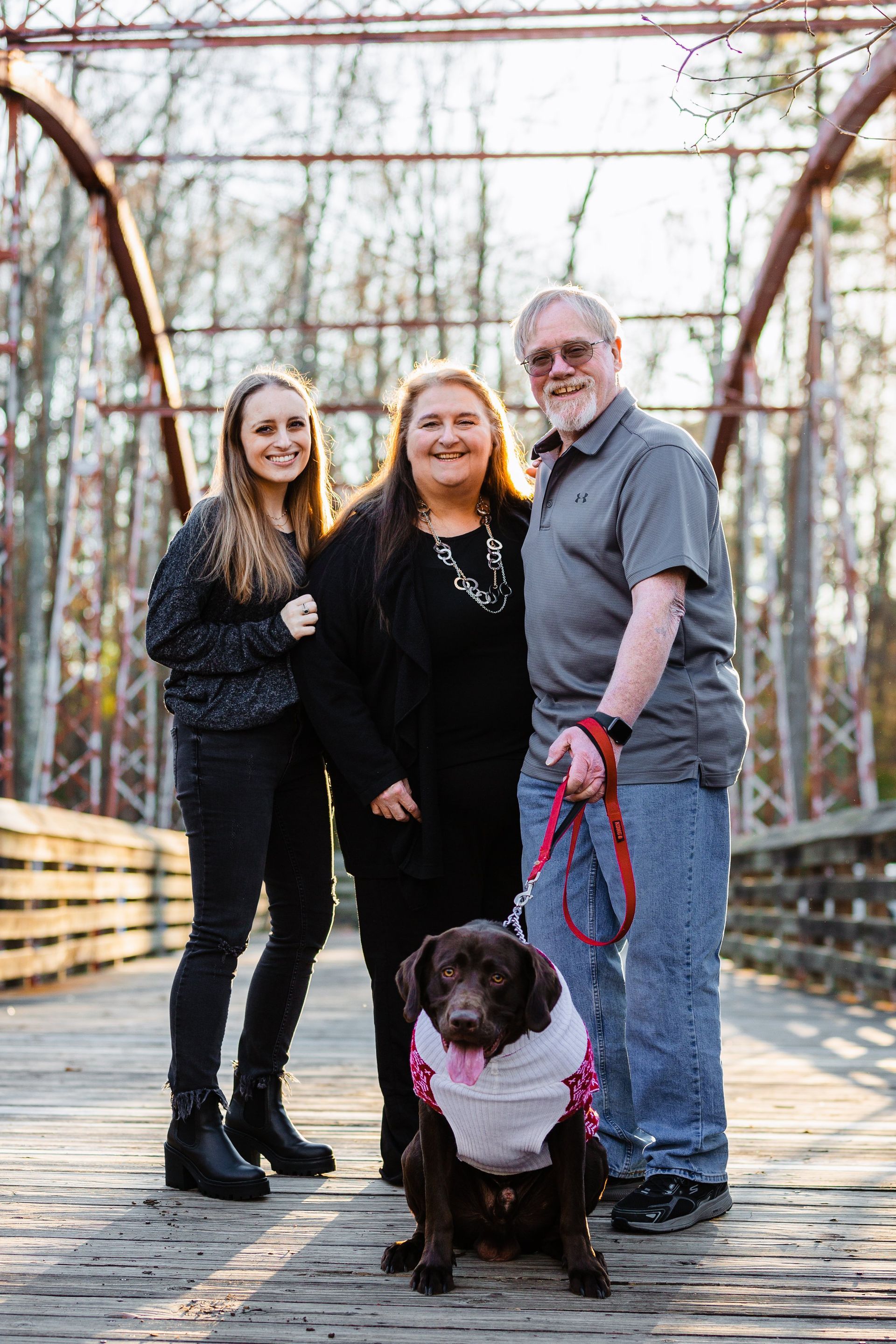 A family is posing for a picture with their dog on a bridge.