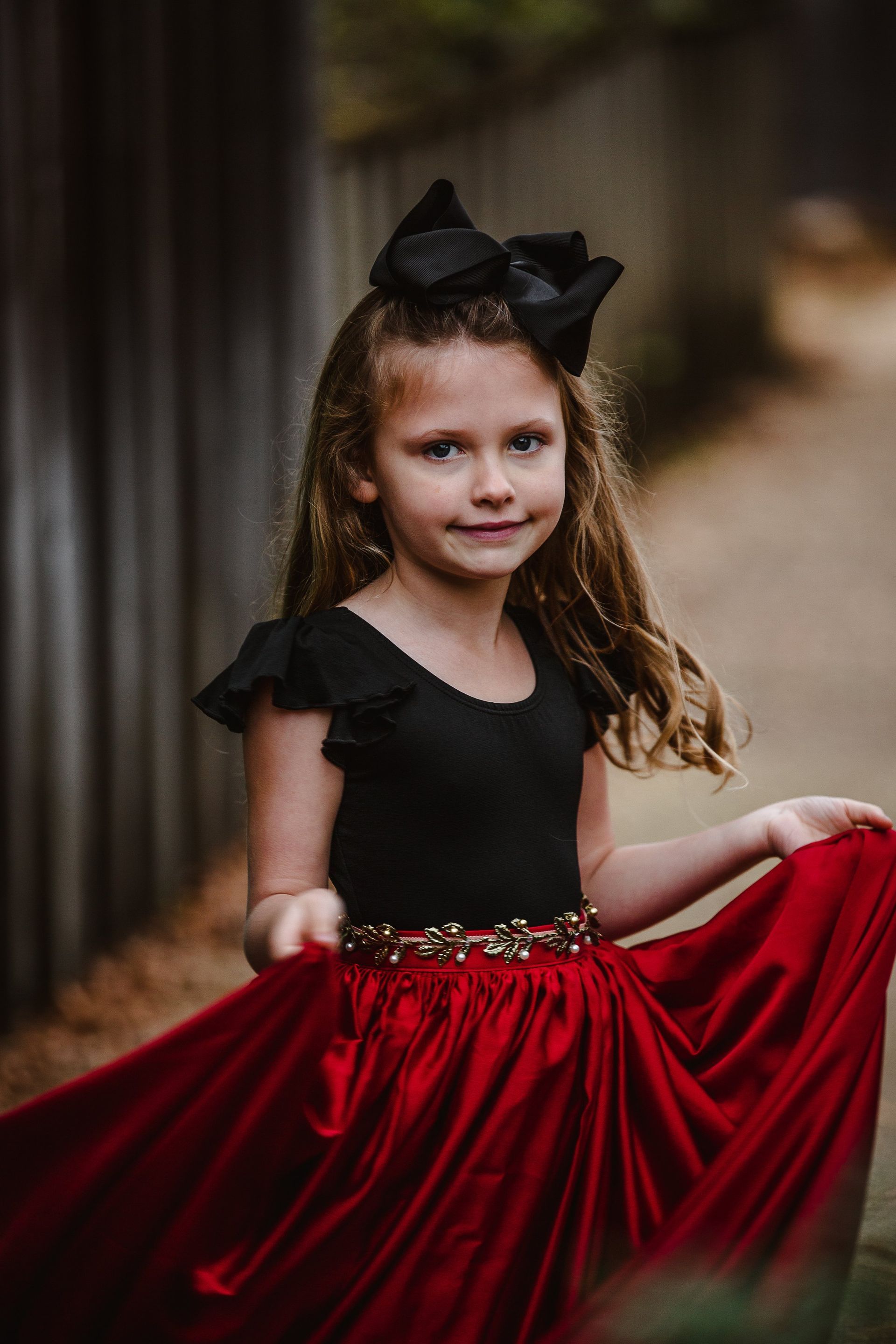 A little girl is wearing a black top and a red skirt.