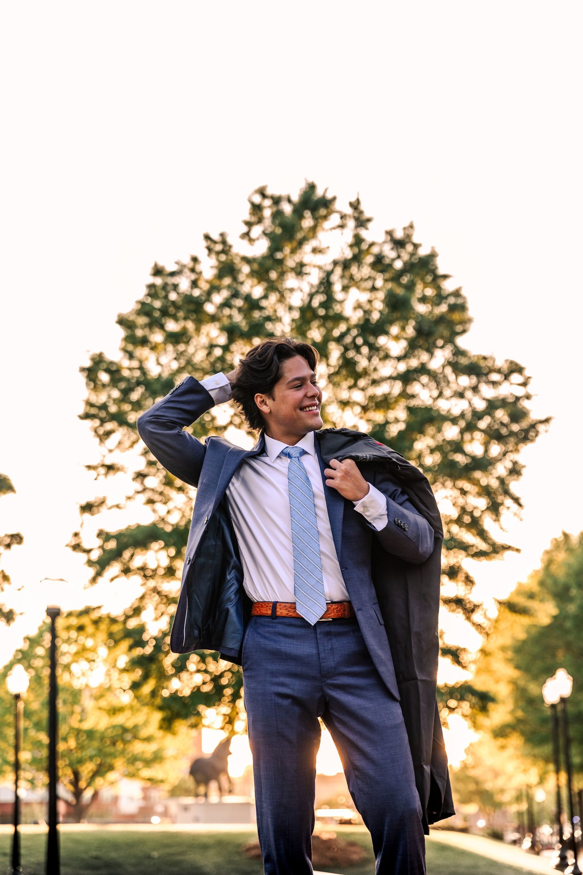 A man in a suit and tie is standing in front of a tree.