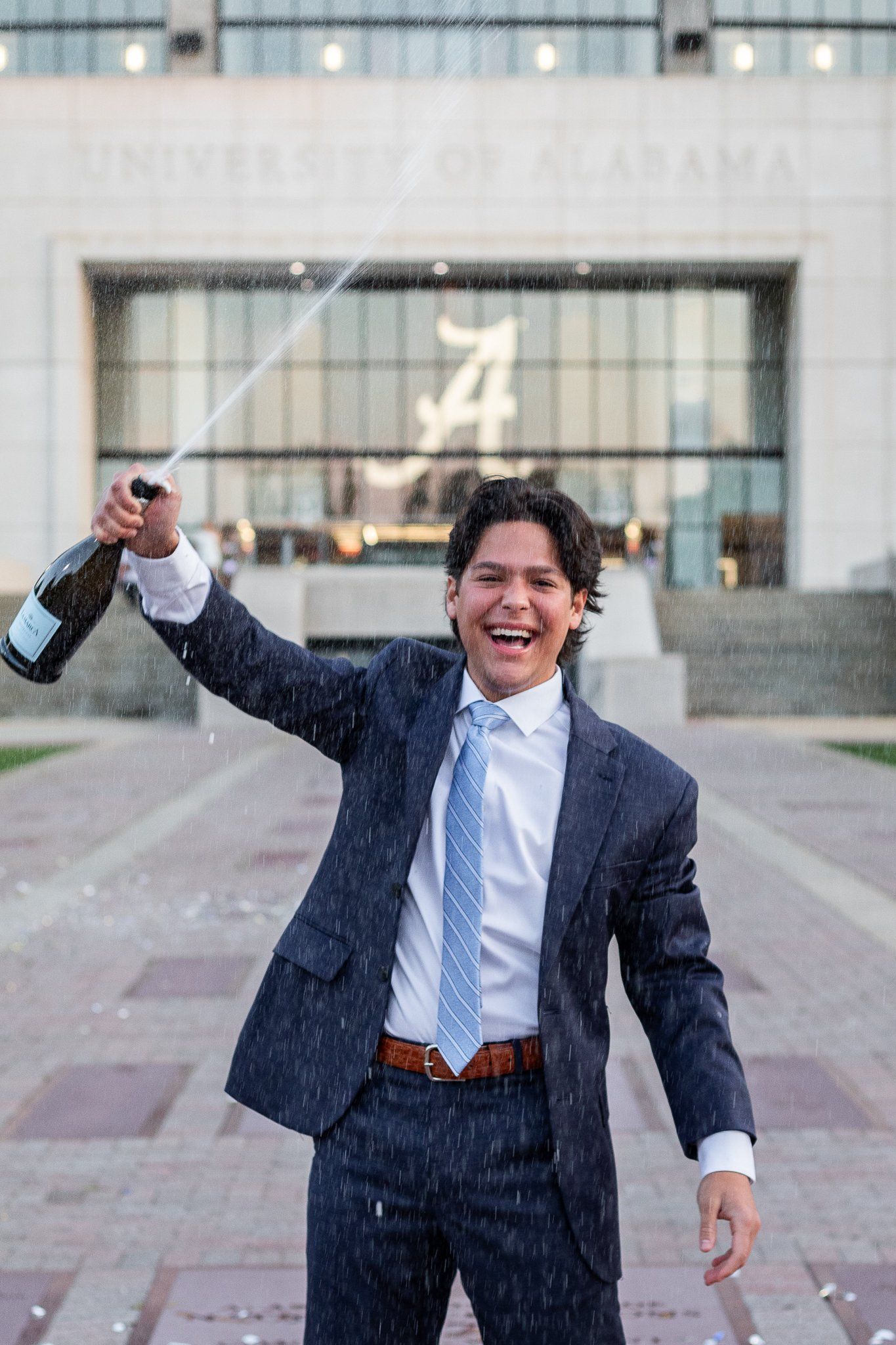 A man in a suit and tie is holding a bottle of champagne in front of a building.