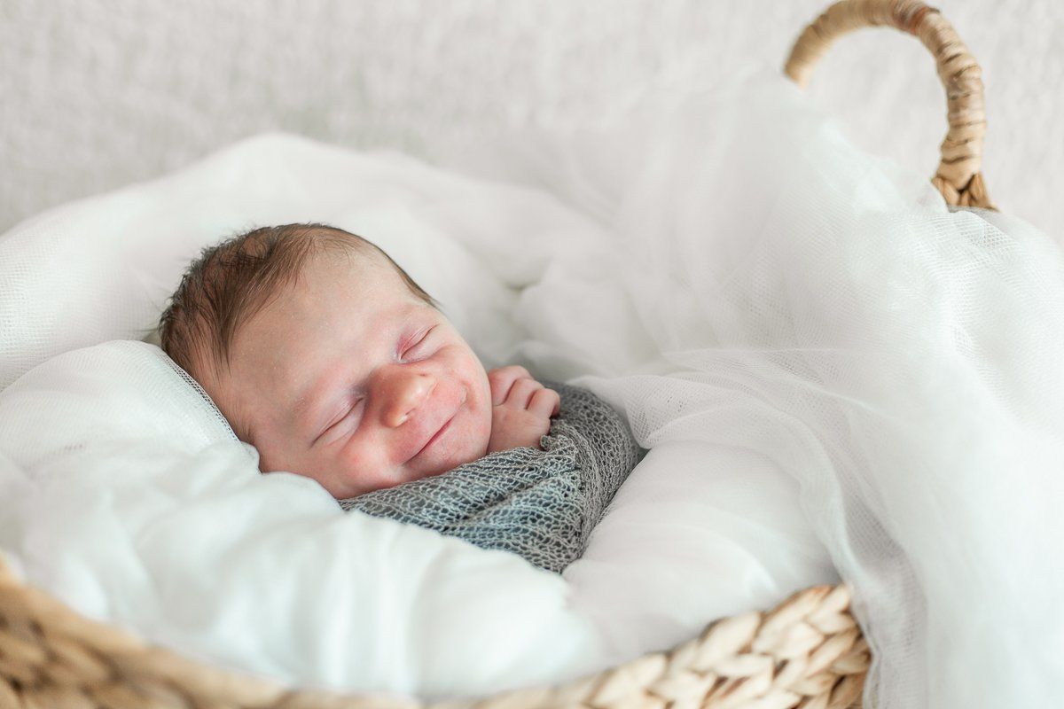 A newborn baby is sleeping in a wicker basket.