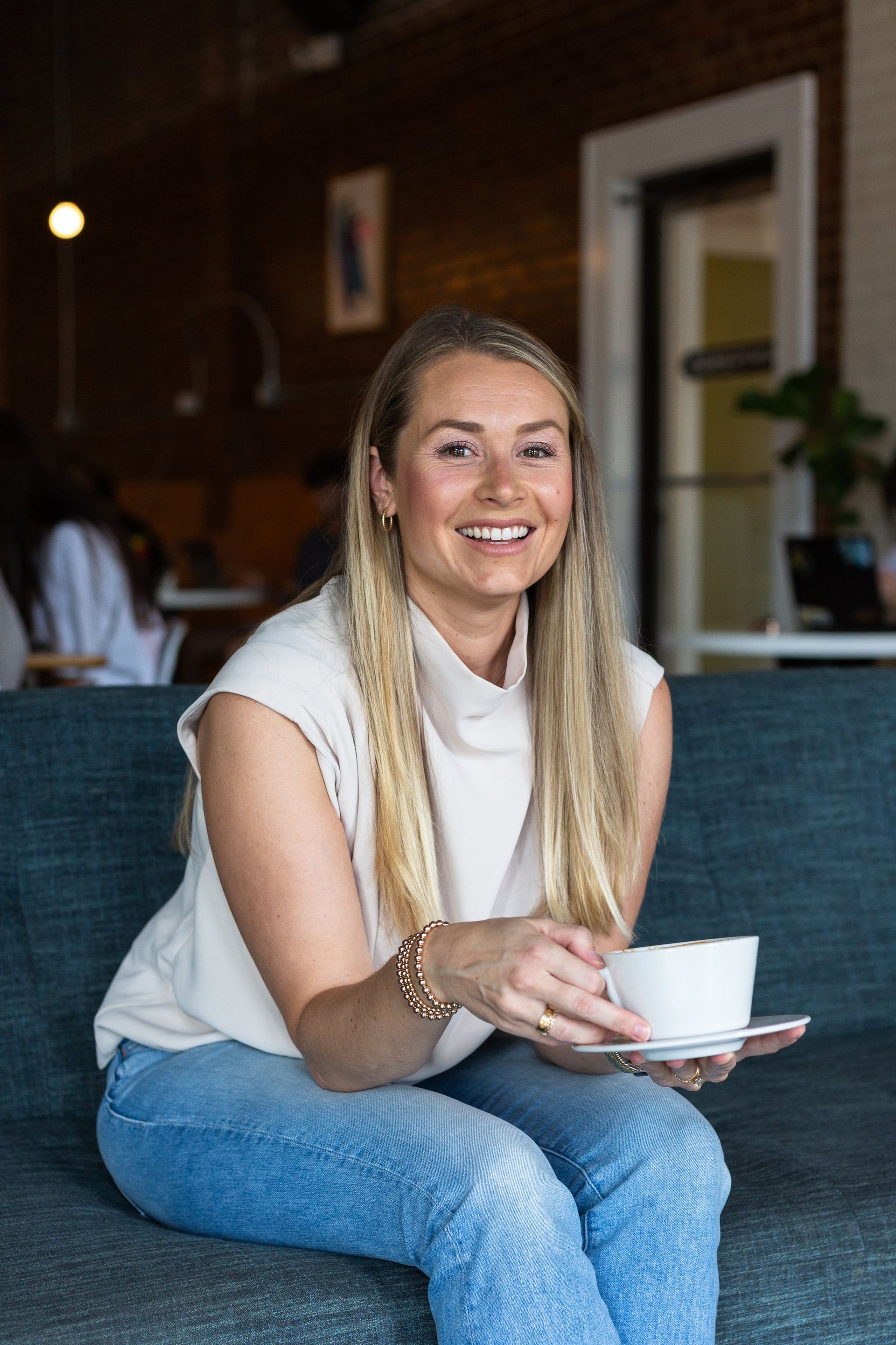 A woman is sitting on a couch holding a cup of coffee.