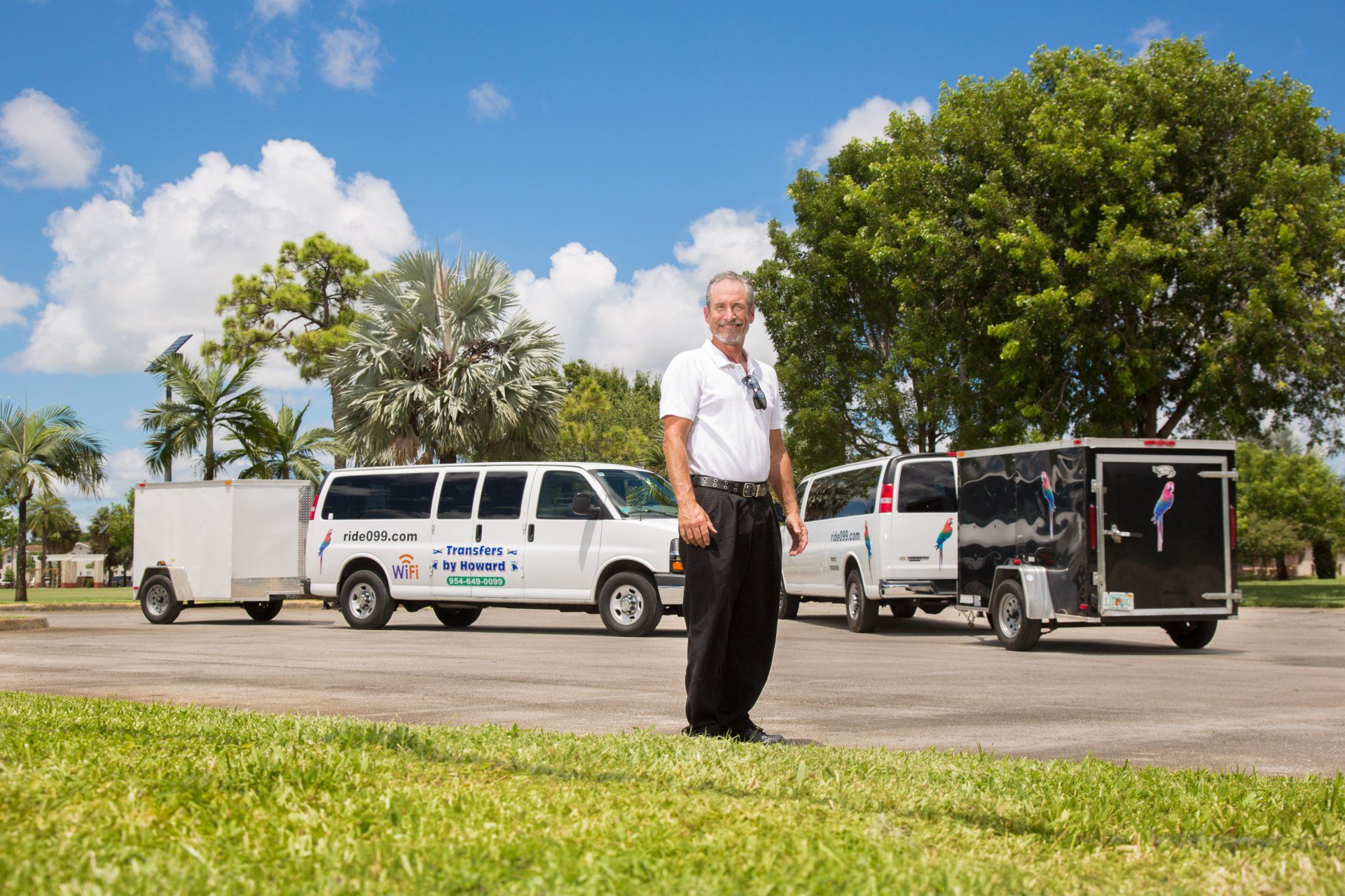 A man is standing in front of a van and trailer in a parking lot.