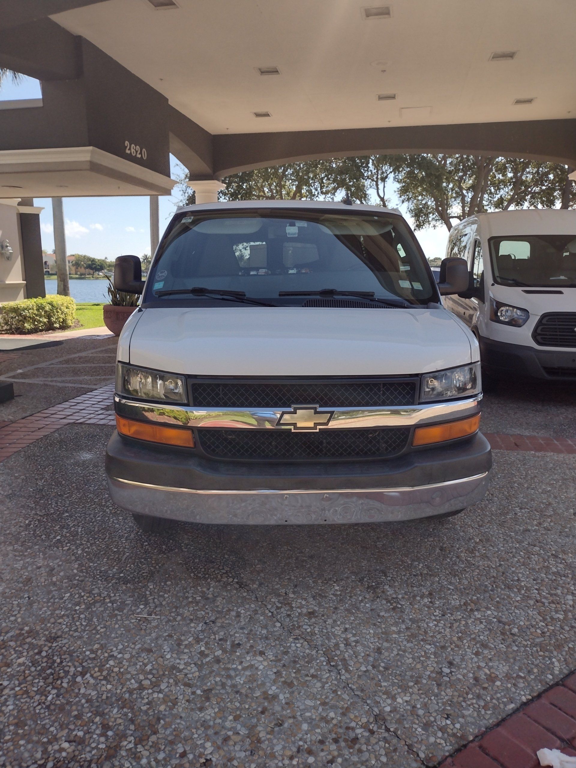 A white chevrolet van is parked in front of a building.