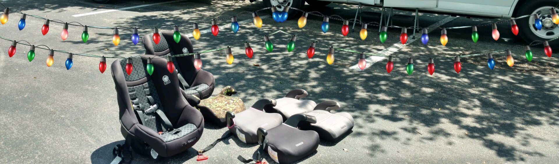 A bunch of car seats are sitting on the ground next to a string of christmas lights.
