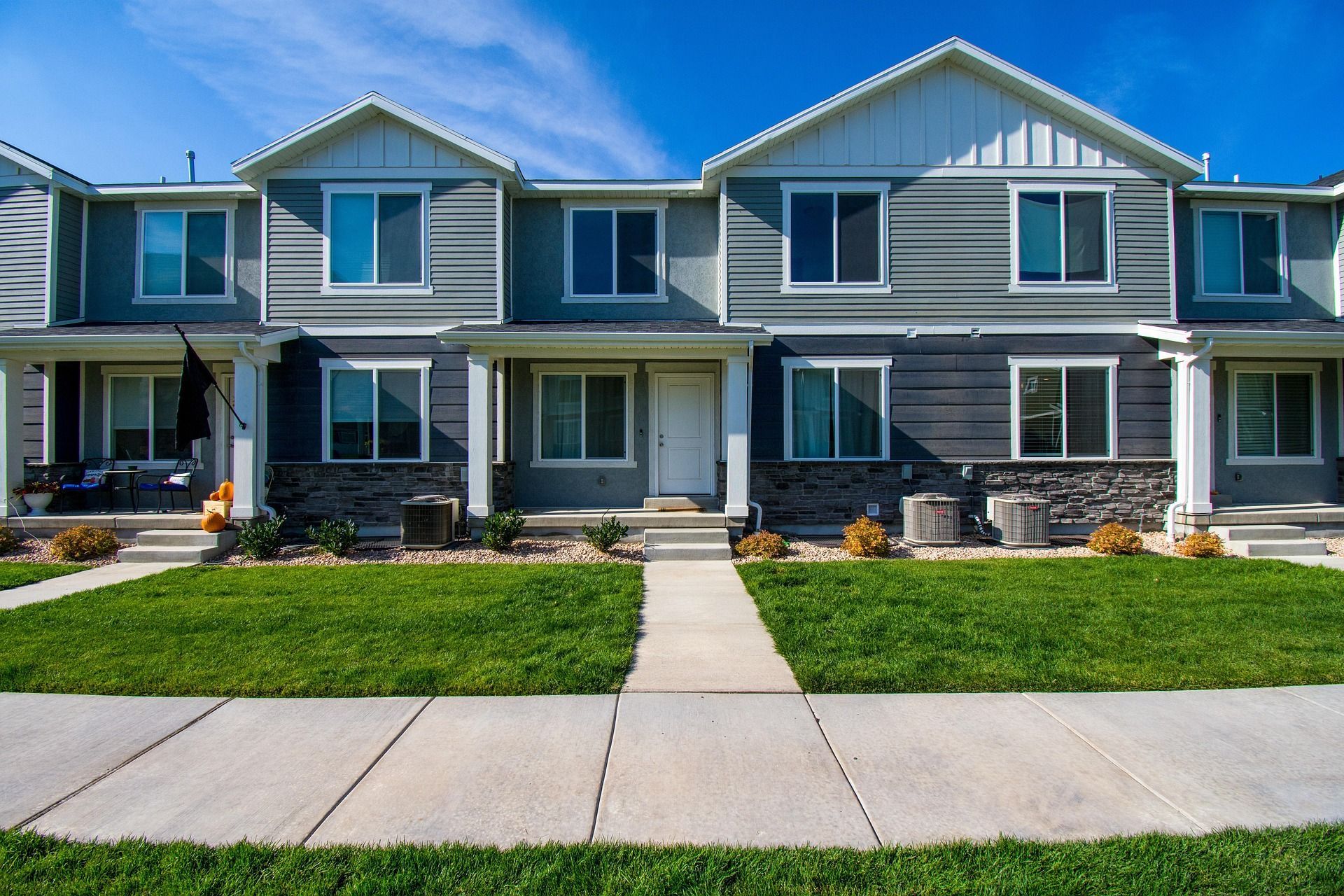 Row of modern gray townhouses with front porches, lawns, and a sidewalk in front