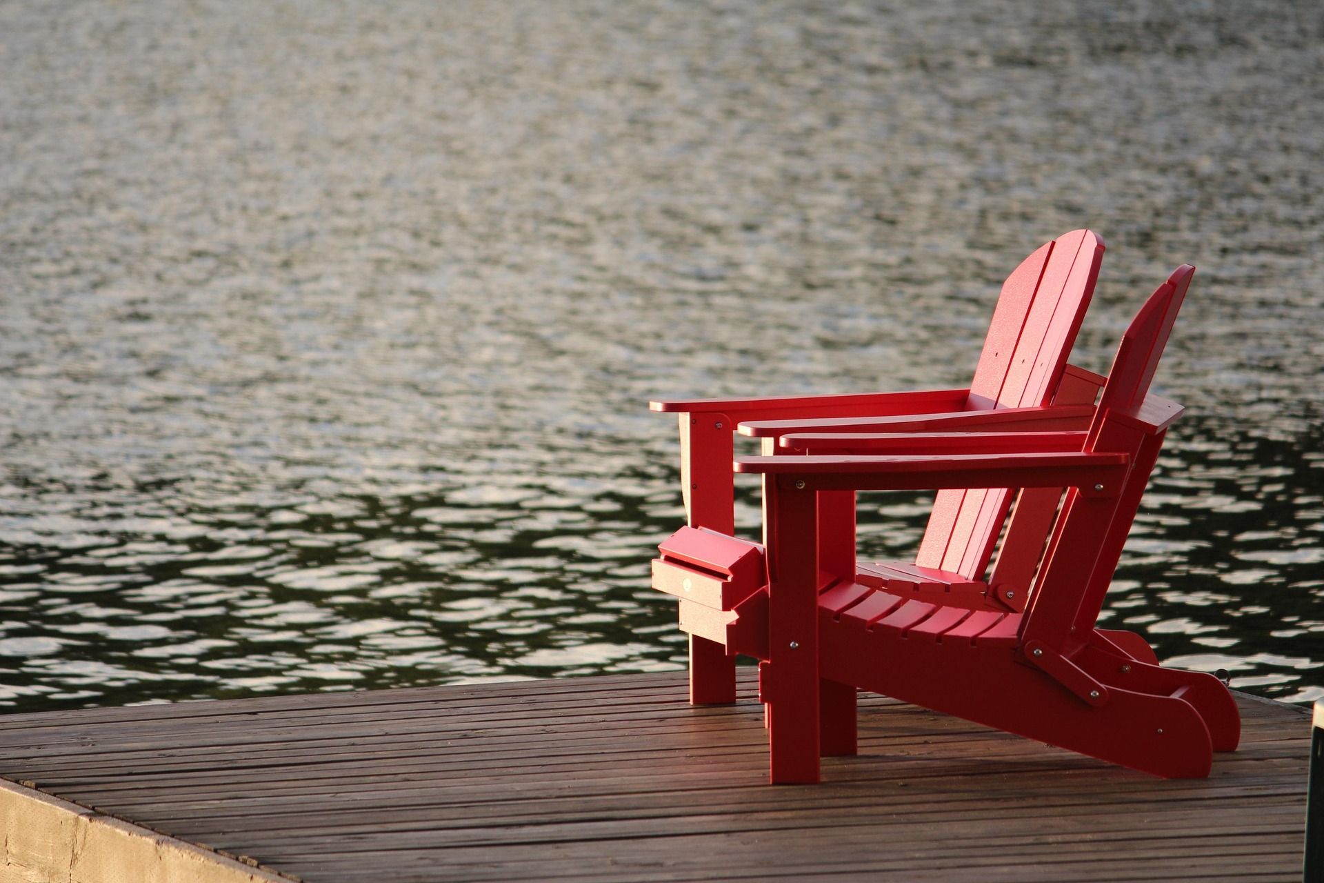 Red Adirondack chair on a wooden dock beside a calm lake