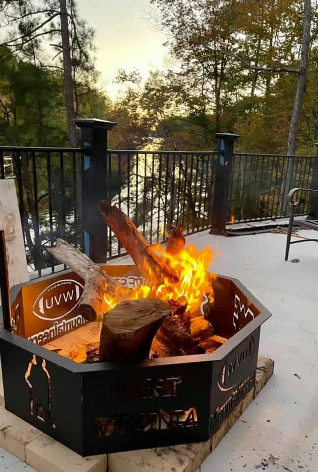 Fire burning in a black metal fire pit on a patio, with logs and a view of Lake Gaston beyond.