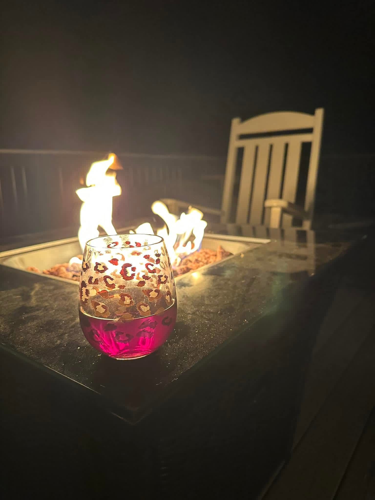 A flaming tabletop fire pit glowing pink beside a chair on a dark patio at night overlooking Lake Gaston