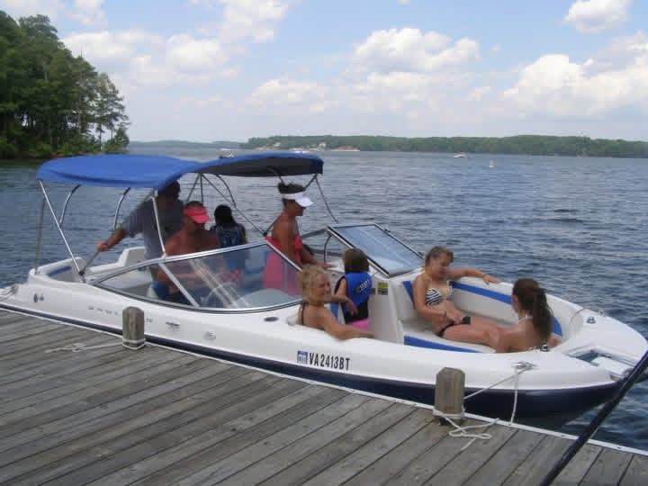 People relaxing on a white speedboat with a blue canopy at a Lake Gaston dock