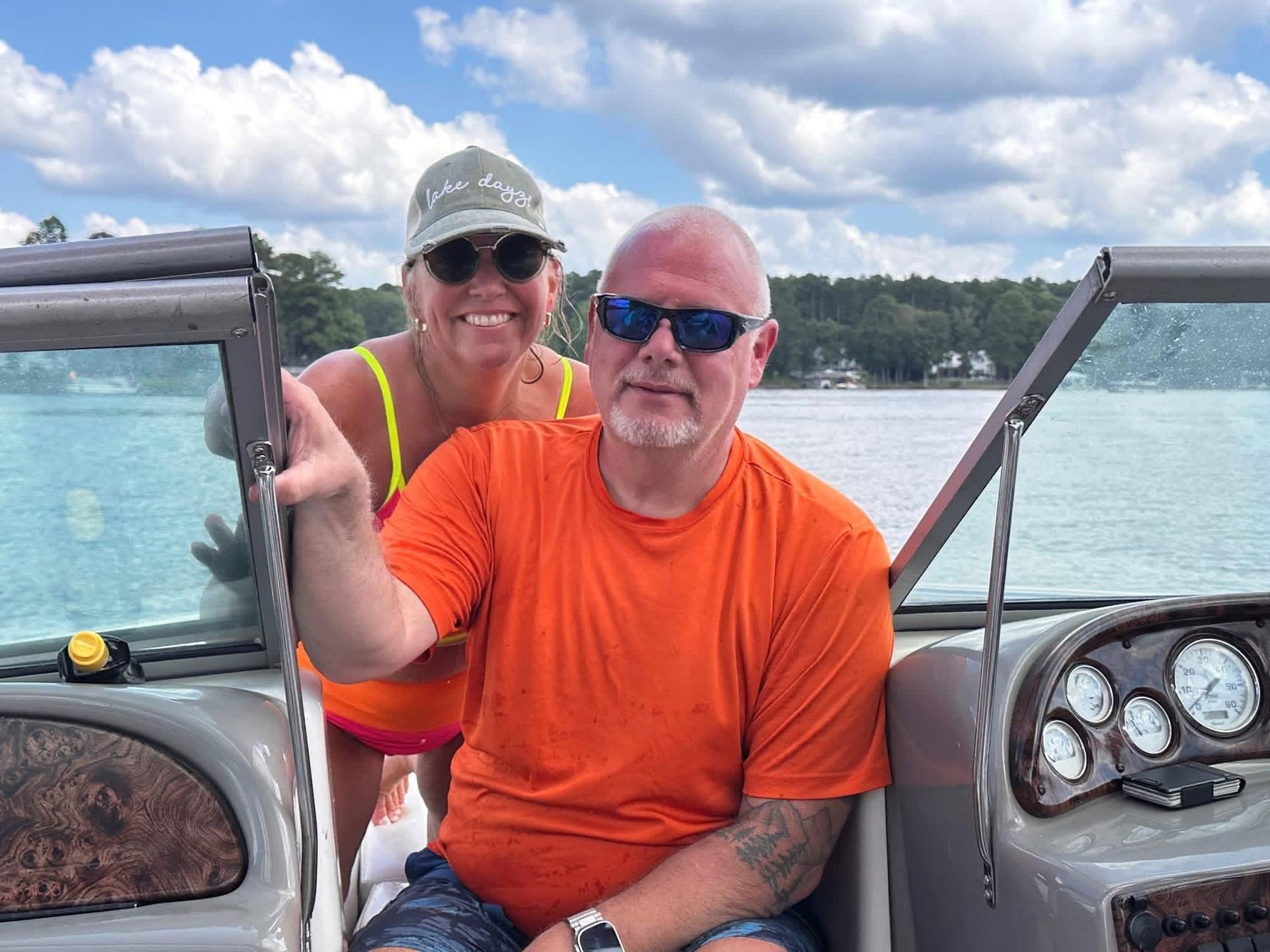 Two people smiling on a boat, wearing sunglasses and bright orange and yellow shirts on Lake Gaston.