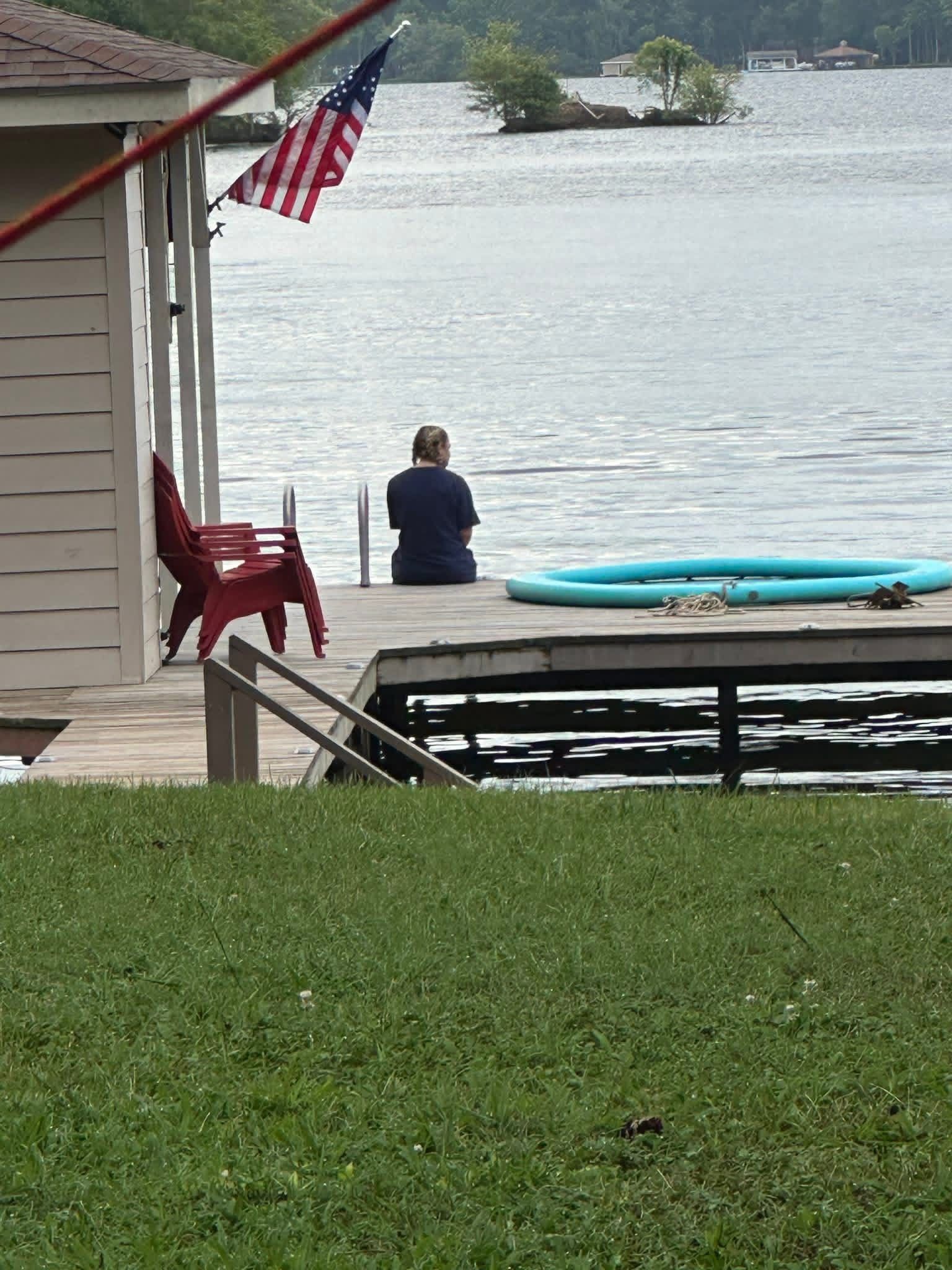 Person sitting at a dock Lake Gaston, with a blue kayak and an American flag nearby.