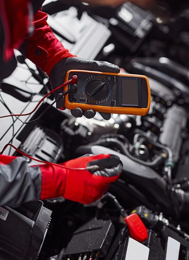 A mechanic is working on a car with a multimeter.