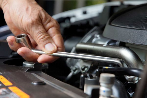 A person is working on a car engine with a wrench.