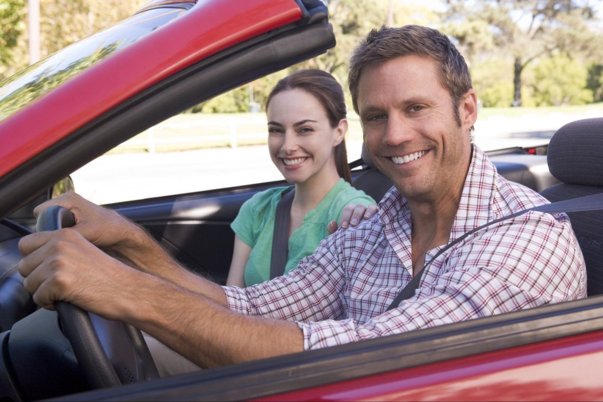 A man and a woman are sitting in a red convertible car.