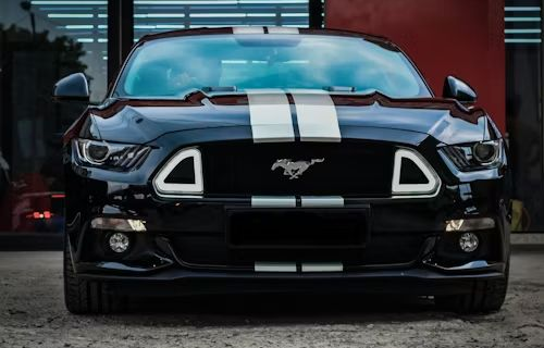 Black Ford Mustang with white racing stripes; parked outdoors.