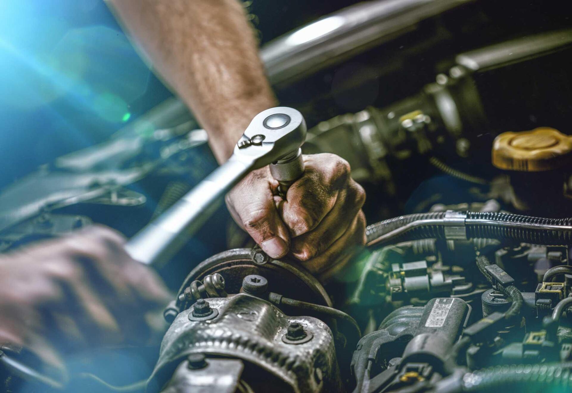 A man is working on a car engine with a wrench.