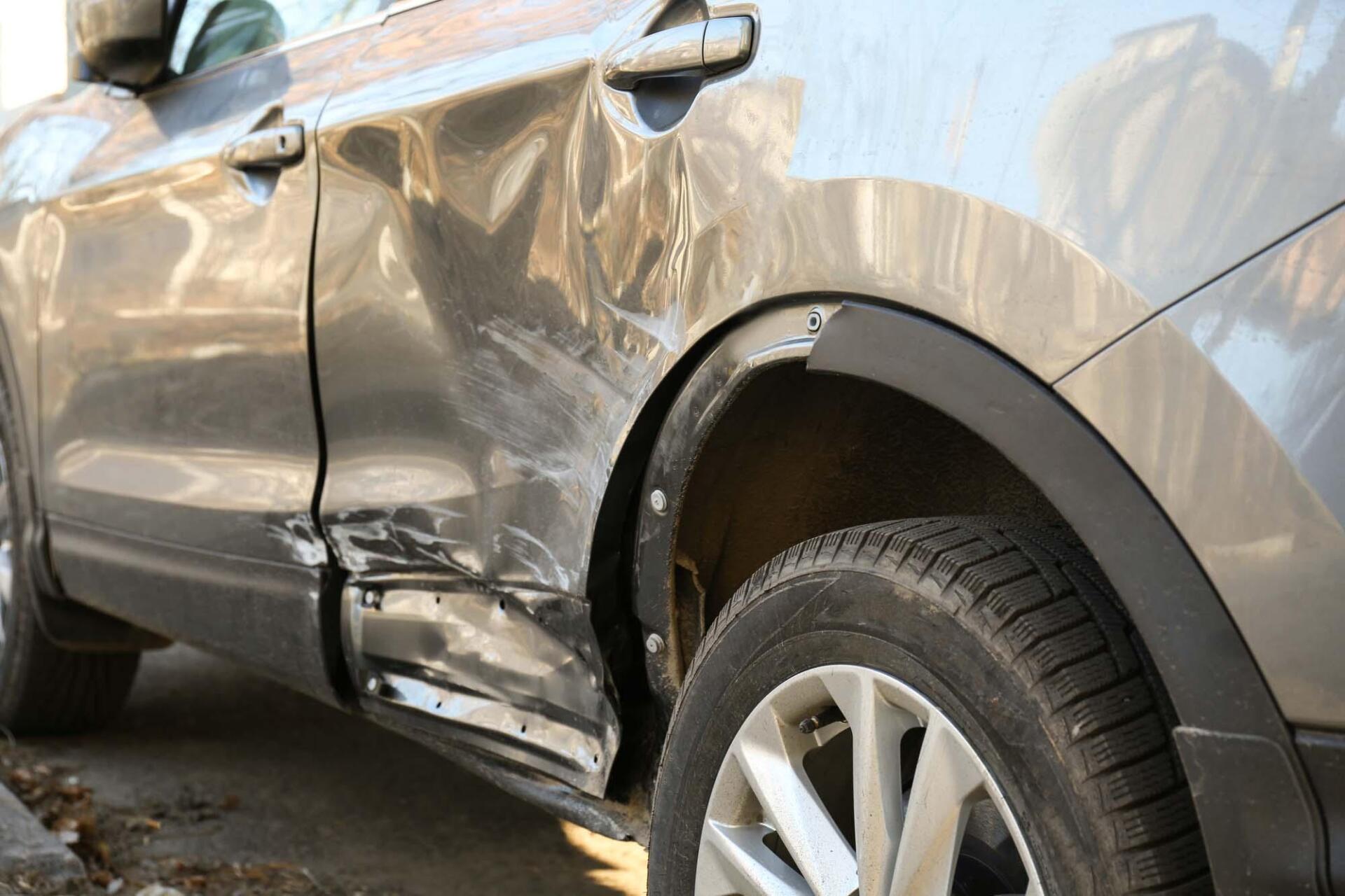 A car with a damaged fender is parked on the side of the road.