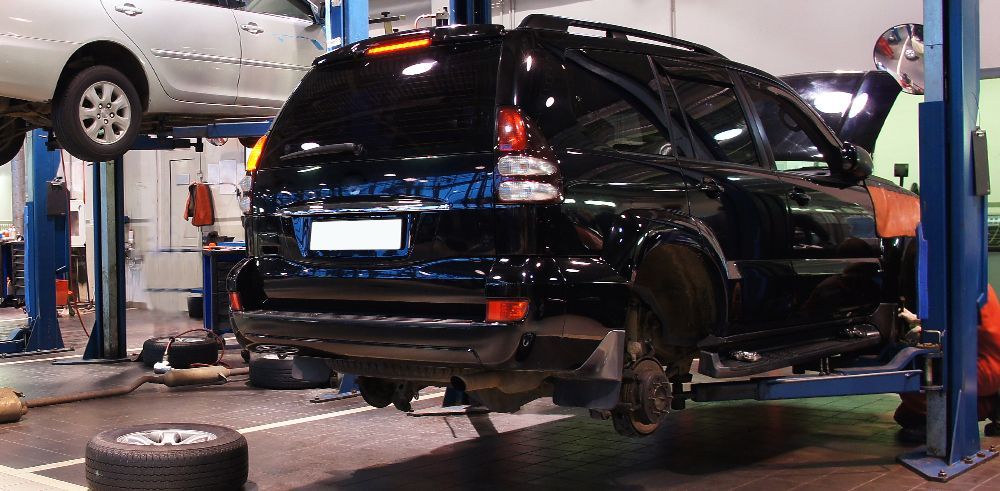 Two cars are sitting on a lift in a garage.