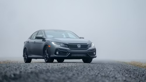 Gray Honda sedan driving on a foggy road with gravel foreground