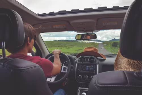 Two people driving a convertible through a green countryside under cloudy skies.