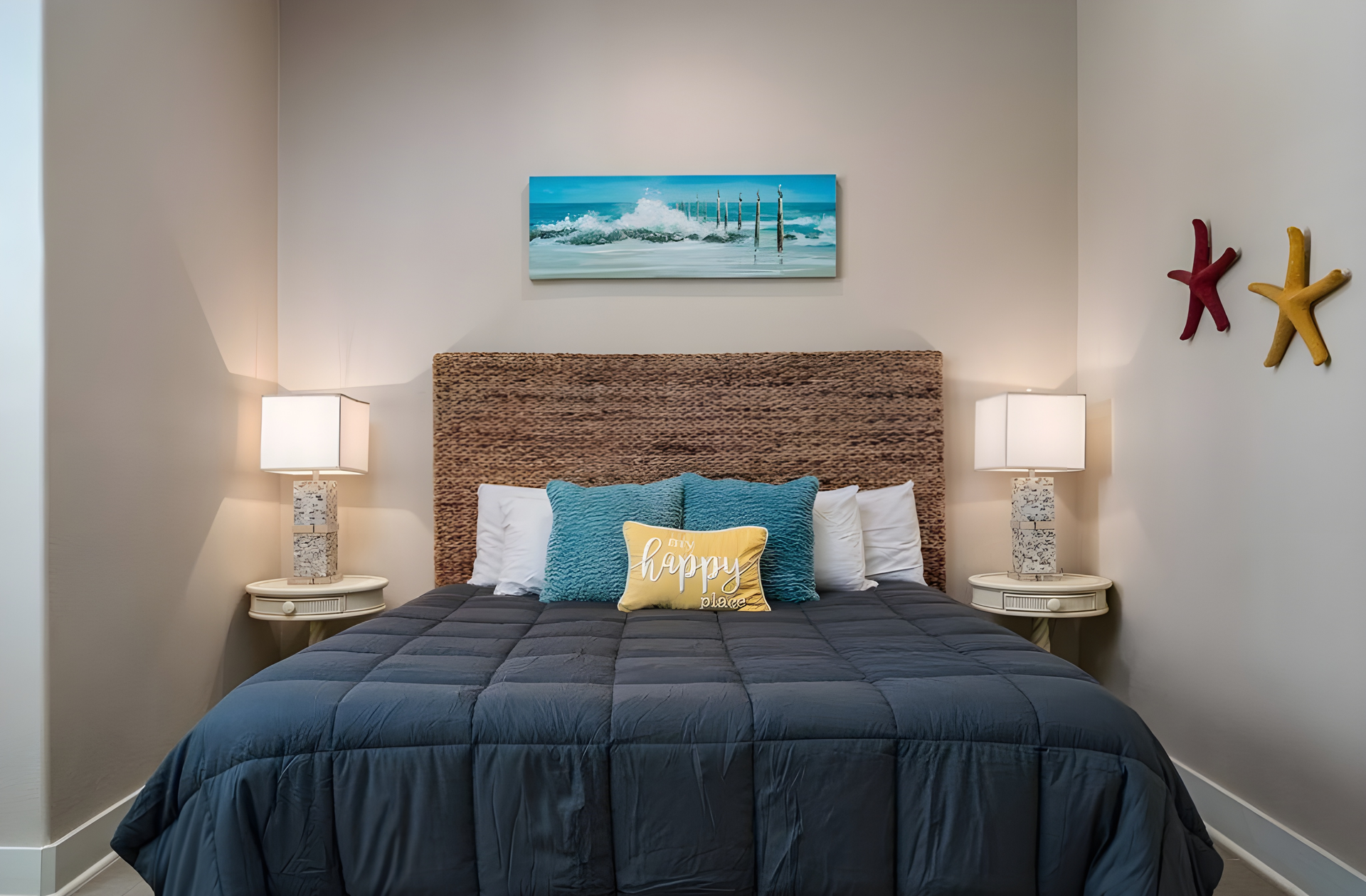 Bedroom with queen bed, lamps, and coastal decor; neutral walls, blue quilt, and starfish accents.