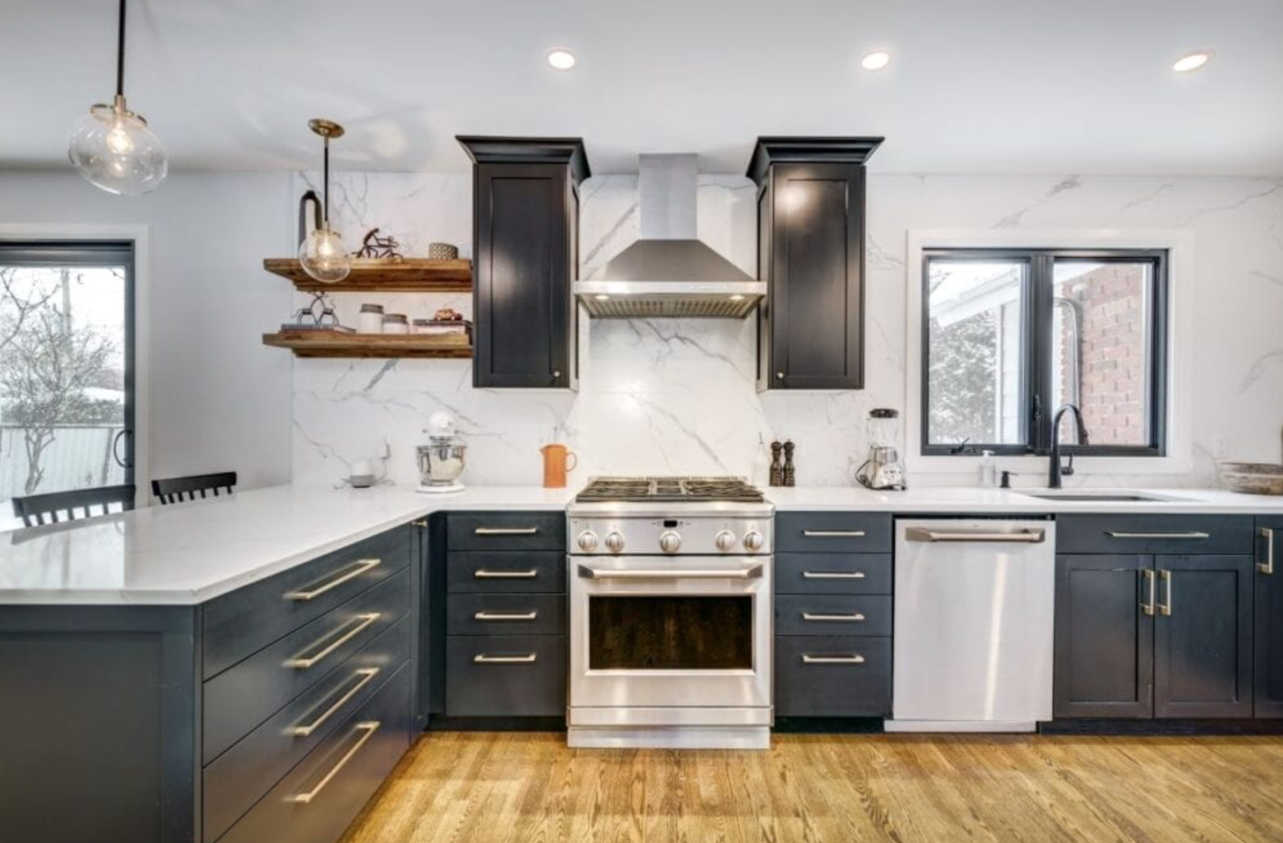 Modern navy blue kitchen with white countertops, stainless steel appliances, and wood floors.