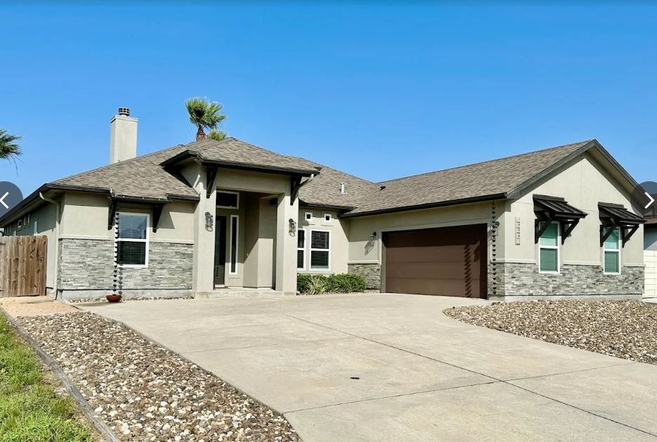 Tan stucco house with stone accents, brown garage door, and driveway under a blue sky.