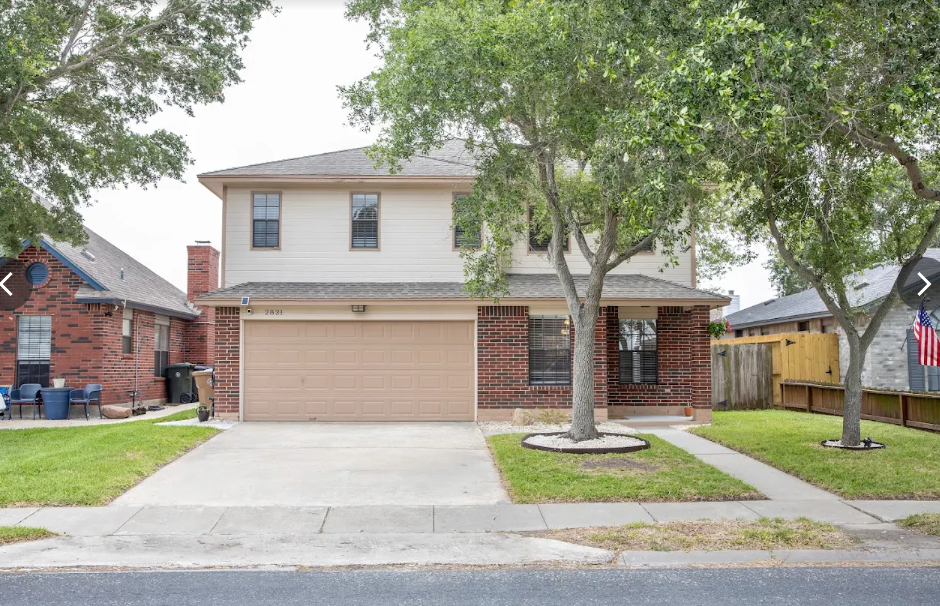 Two-story house with brick and beige siding, garage, and trees on the front lawn.