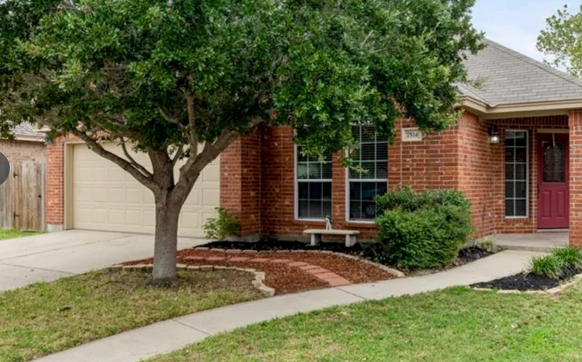 Brick house with tree, pathway, and lawn. Brown brick, beige garage door, and red front door.