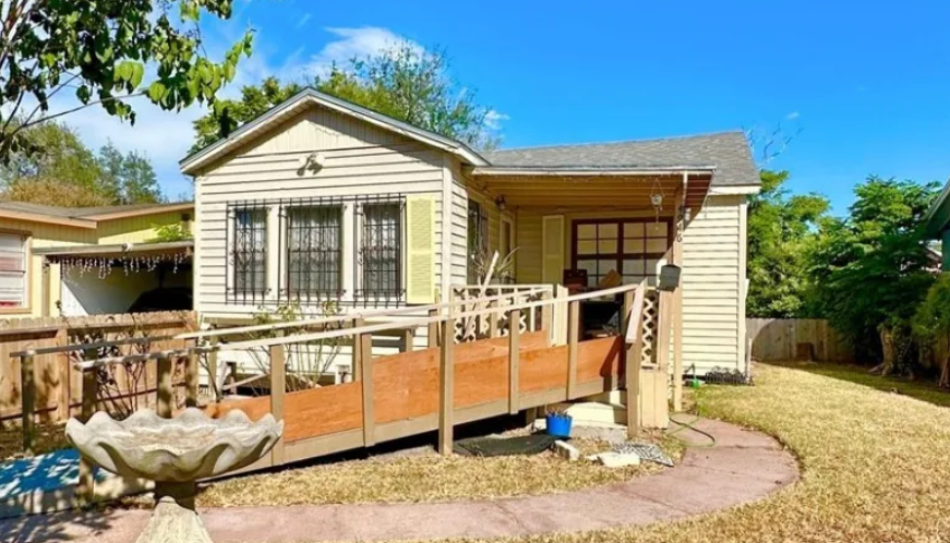 Tan house with wheelchair ramp, bird bath, and green lawn. Sunny day.