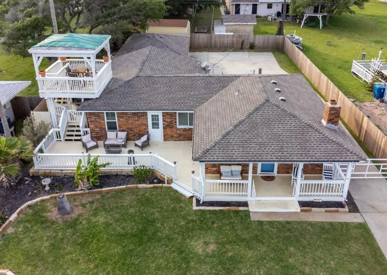 Aerial view of a brick house with a deck, balcony, and gazebo on a grassy lot.
